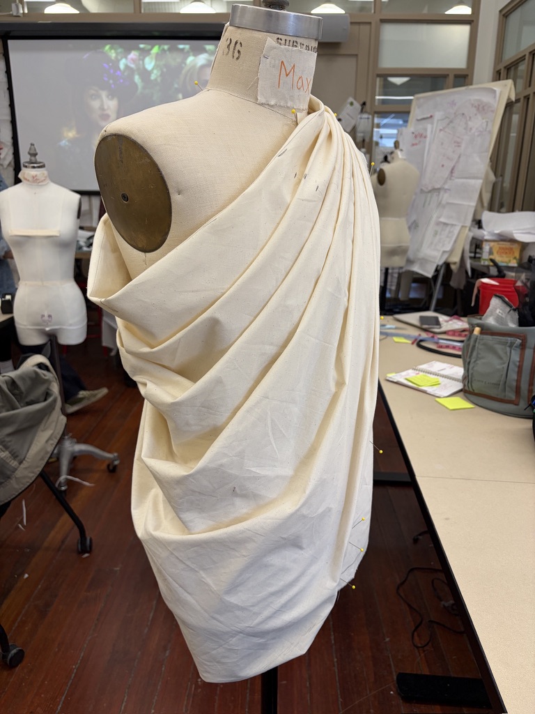 Cream cloth draped asymmetrically across a dress form in the fashion studio