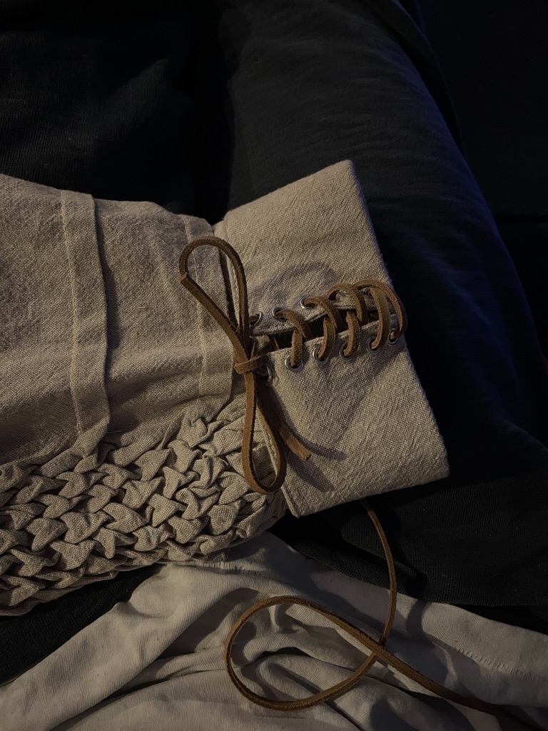 Linen sleeve detail combining hand-smocked texture with a leather-laced cuff