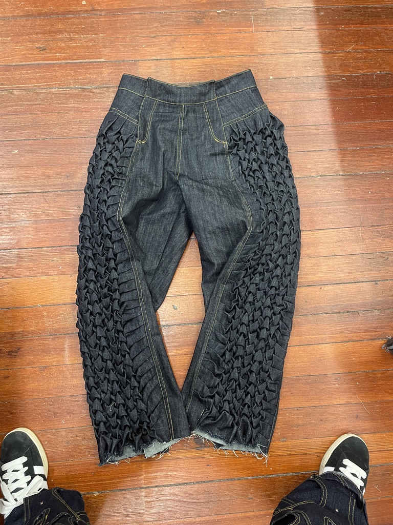 Partially constructed dark denim trousers with smocked panels along both outer legs