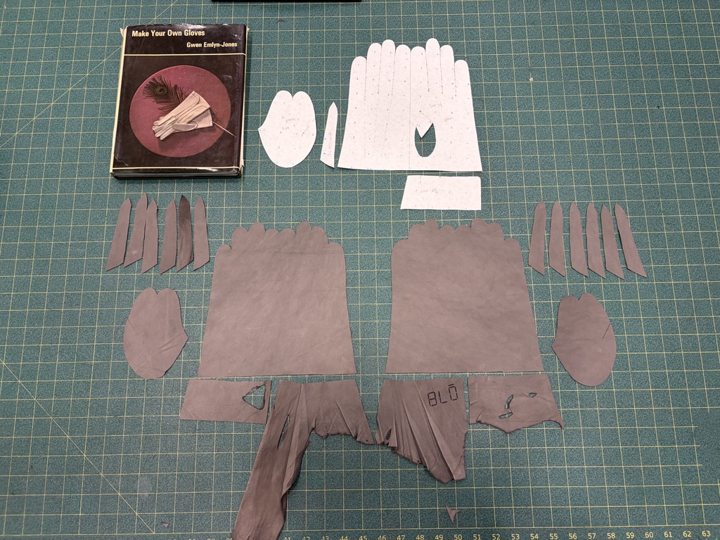 Paper glove pattern and cut fabric pieces arranged on a gridded cutting mat