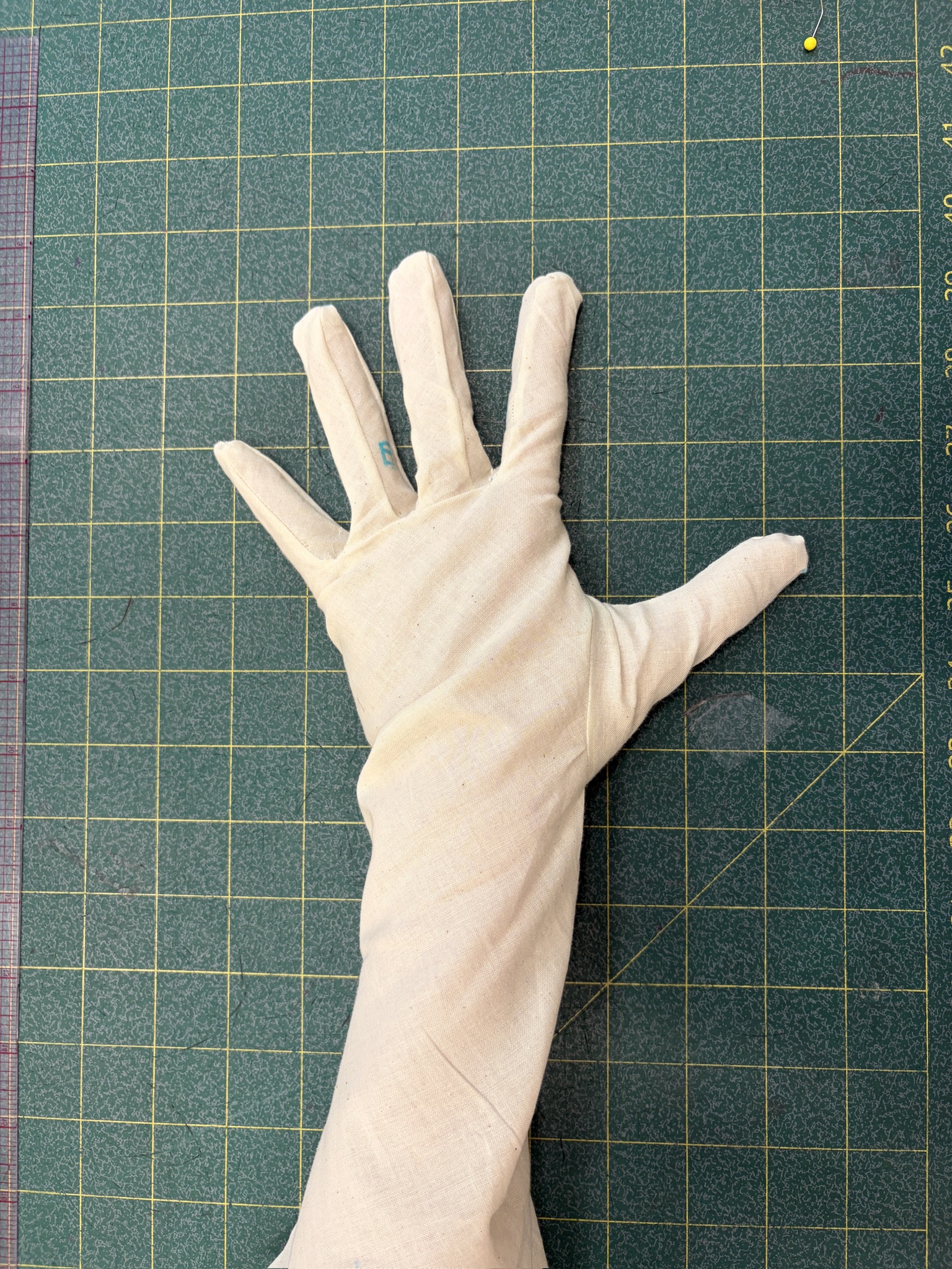 Completed cream fabric glove prototype resting on the cutting mat