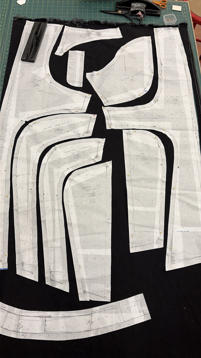 Hand-annotated garment patterns pinned over black fabric on a cutting table