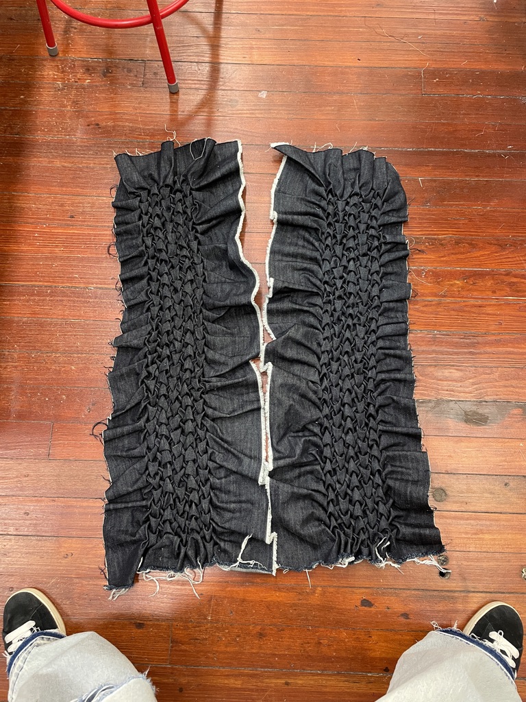 Two unfinished denim panels densely smocked by hand and laid on a studio floor