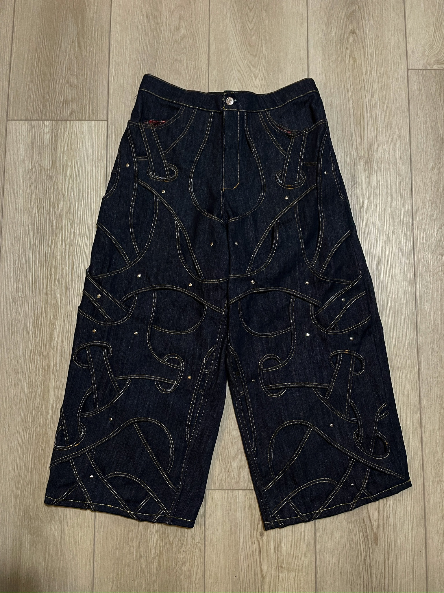 Dark indigo jeans covered with looping applied denim bands and metal studs