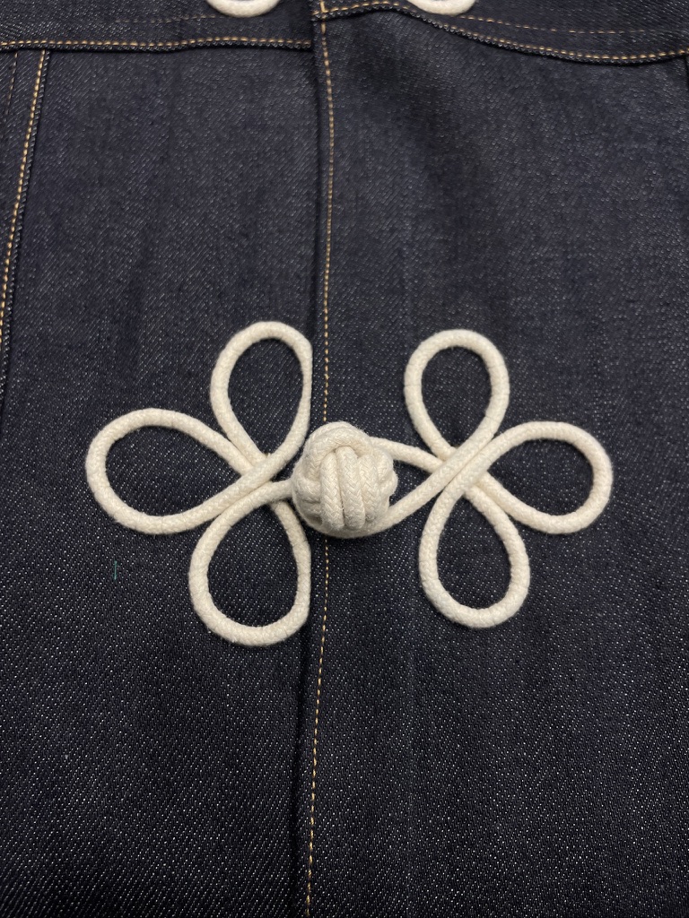 Close view of an oversized white frog closure fixed to dark indigo denim